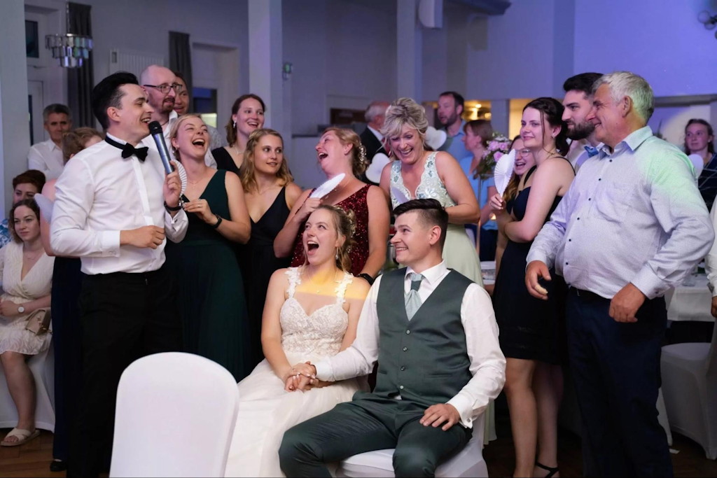 Hochzeitsmoderator mit Mikrofon unterh&auml;lt die G&auml;ste an den festlich gedeckten Tischen